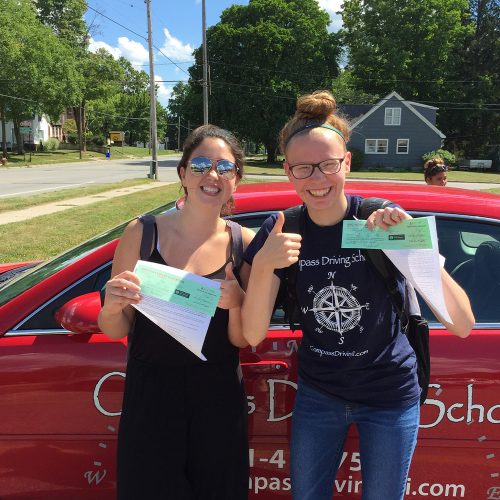 Two female Compass driving students holding up certificates excitedly
